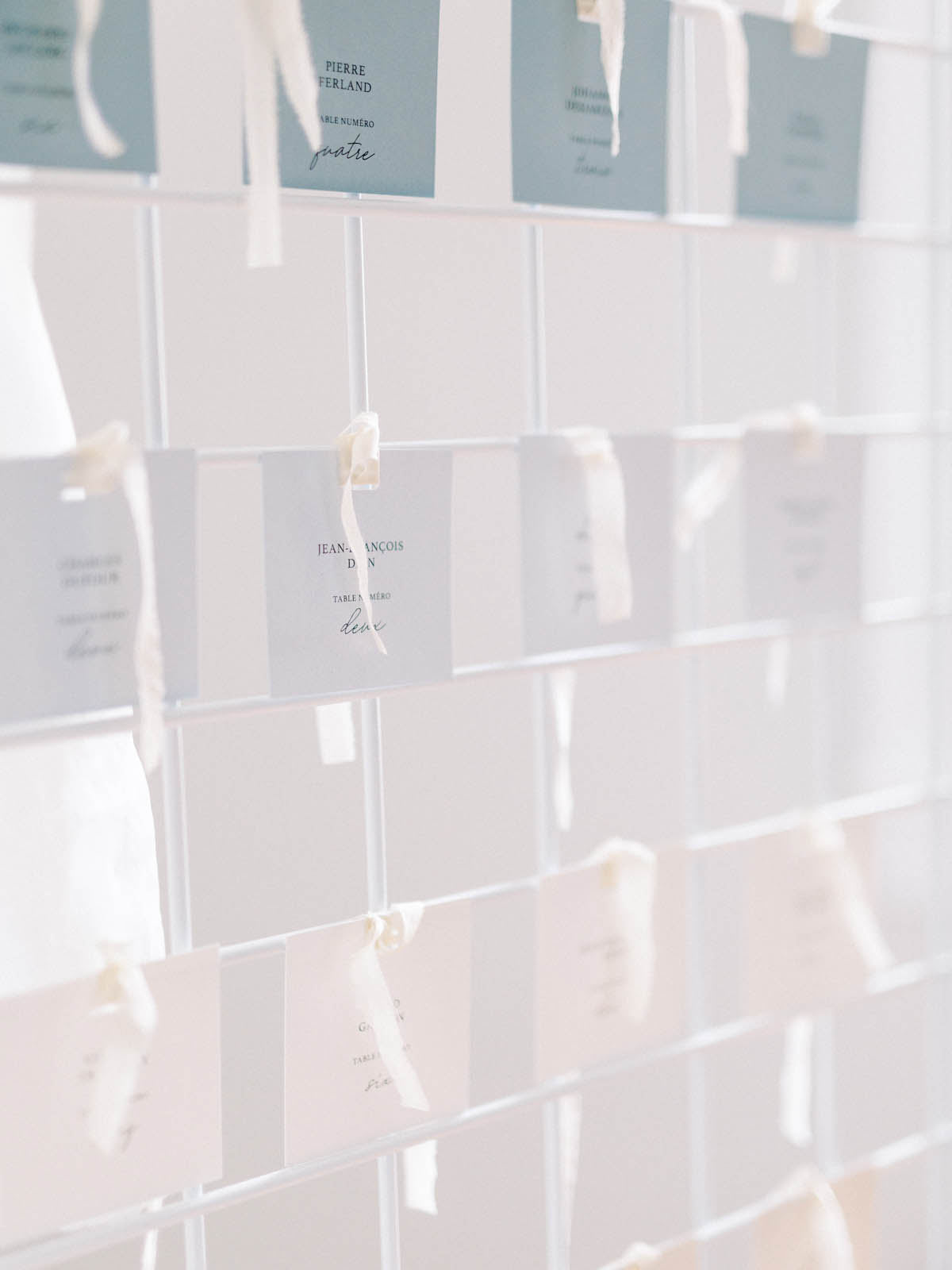 Escort cards tied with silk ribbon to an acrylic display wall