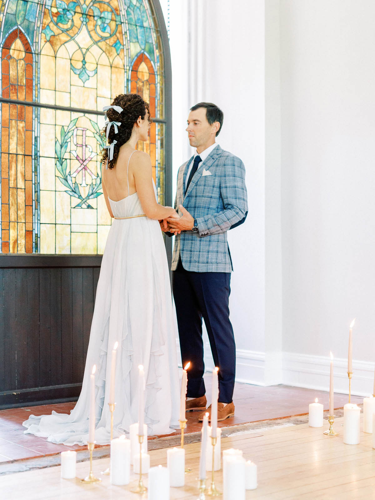 Couple holding hands during the ceremony in front of a stained glass window