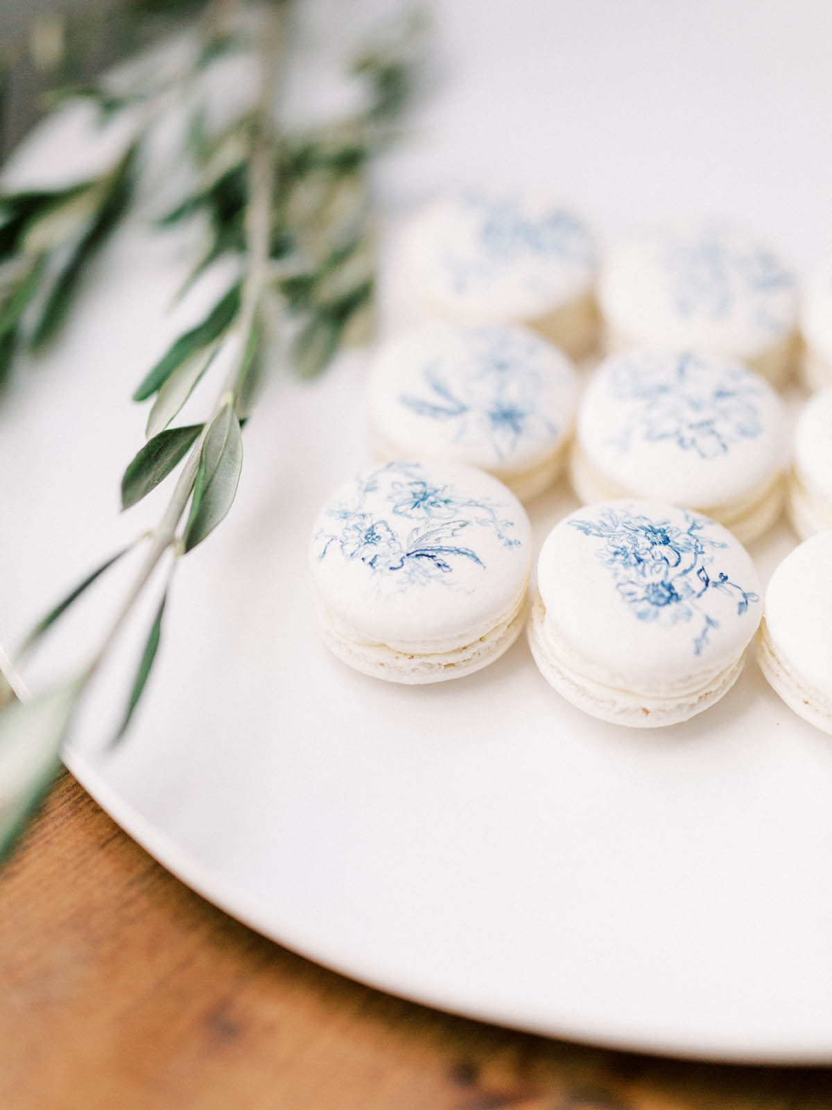 White macarons printed with a blue toile floral motif beside olive branches