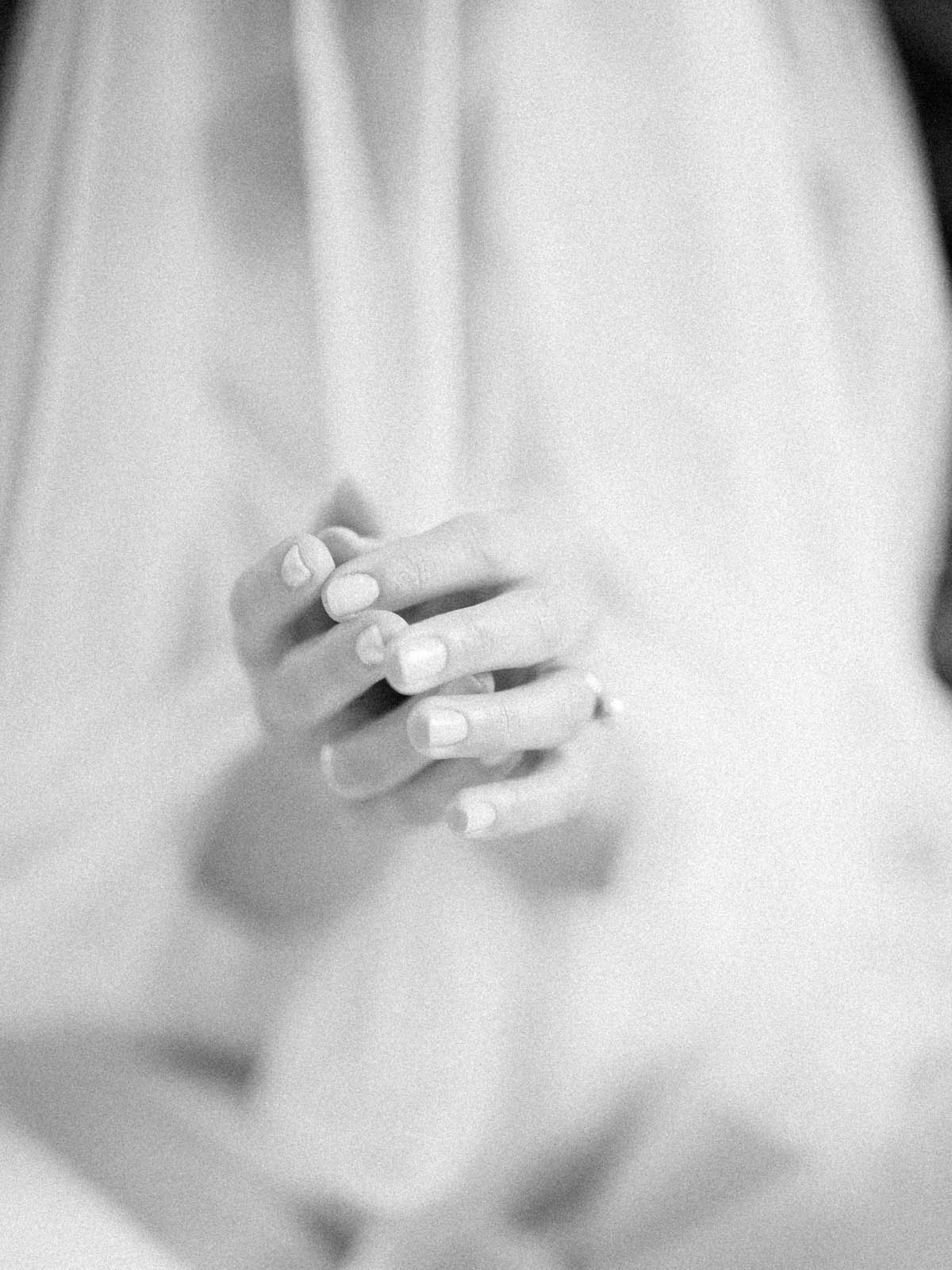 Soft focus detail of the bride's clasped hands against her gown