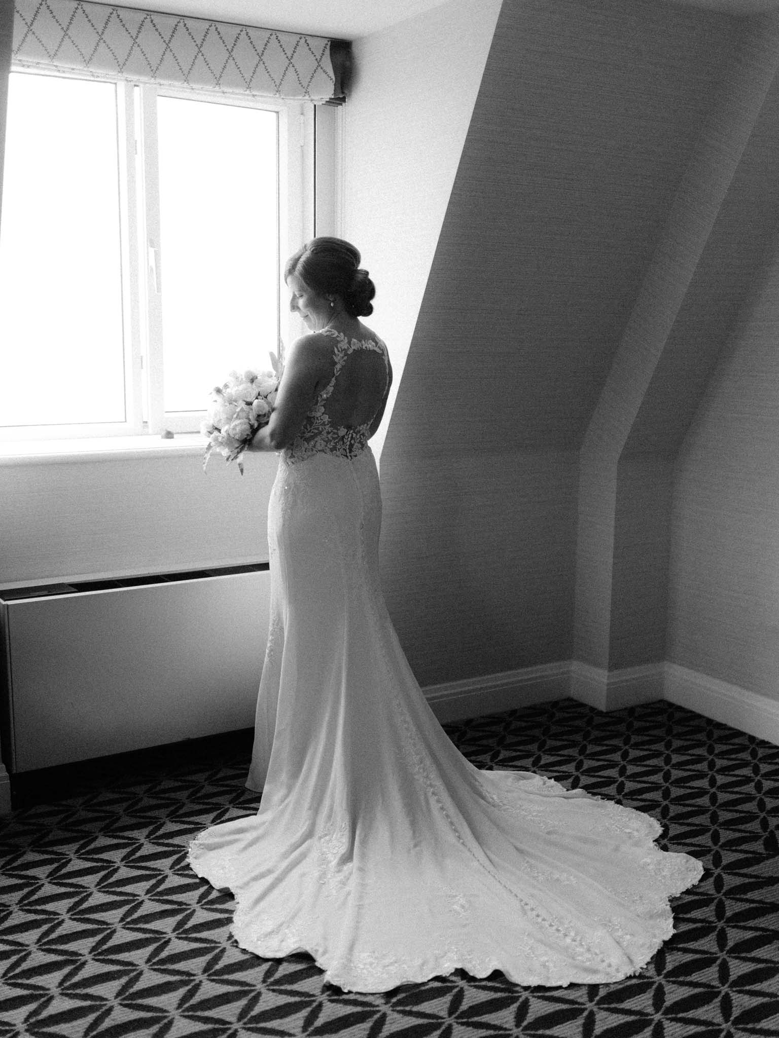 Bride at the window of her room at Fairmont Le Manoir Richelieu, holding her white peony bouquet