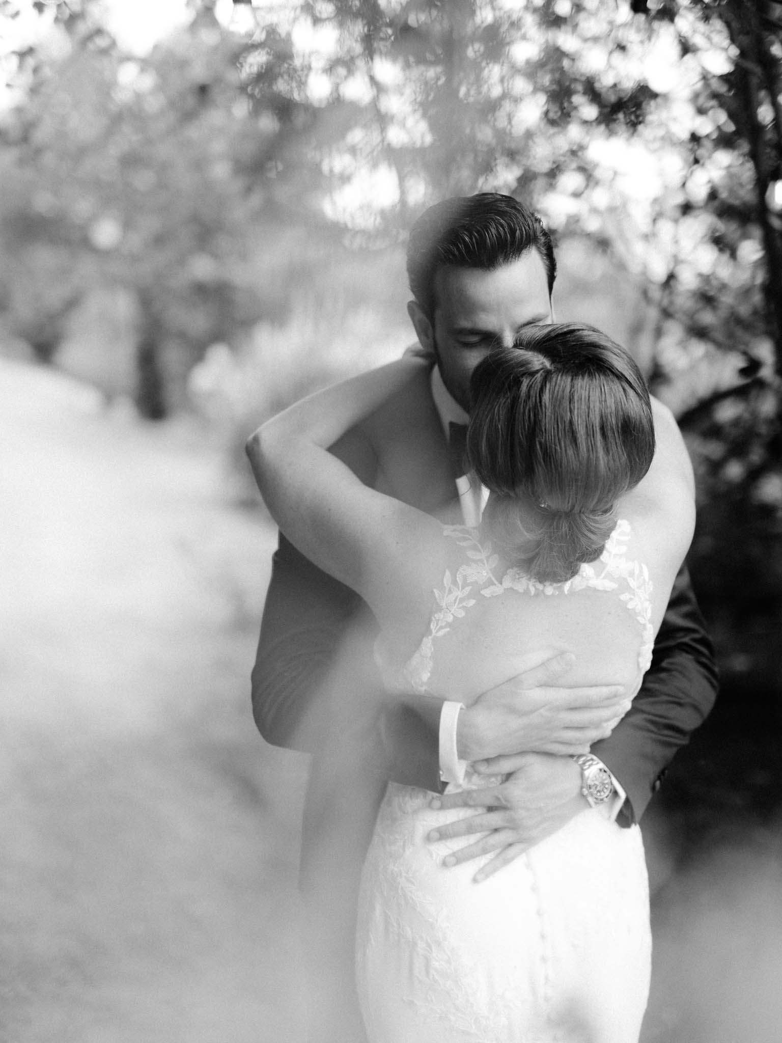 Black and white photograph of the bride and groom holding each other under the trees