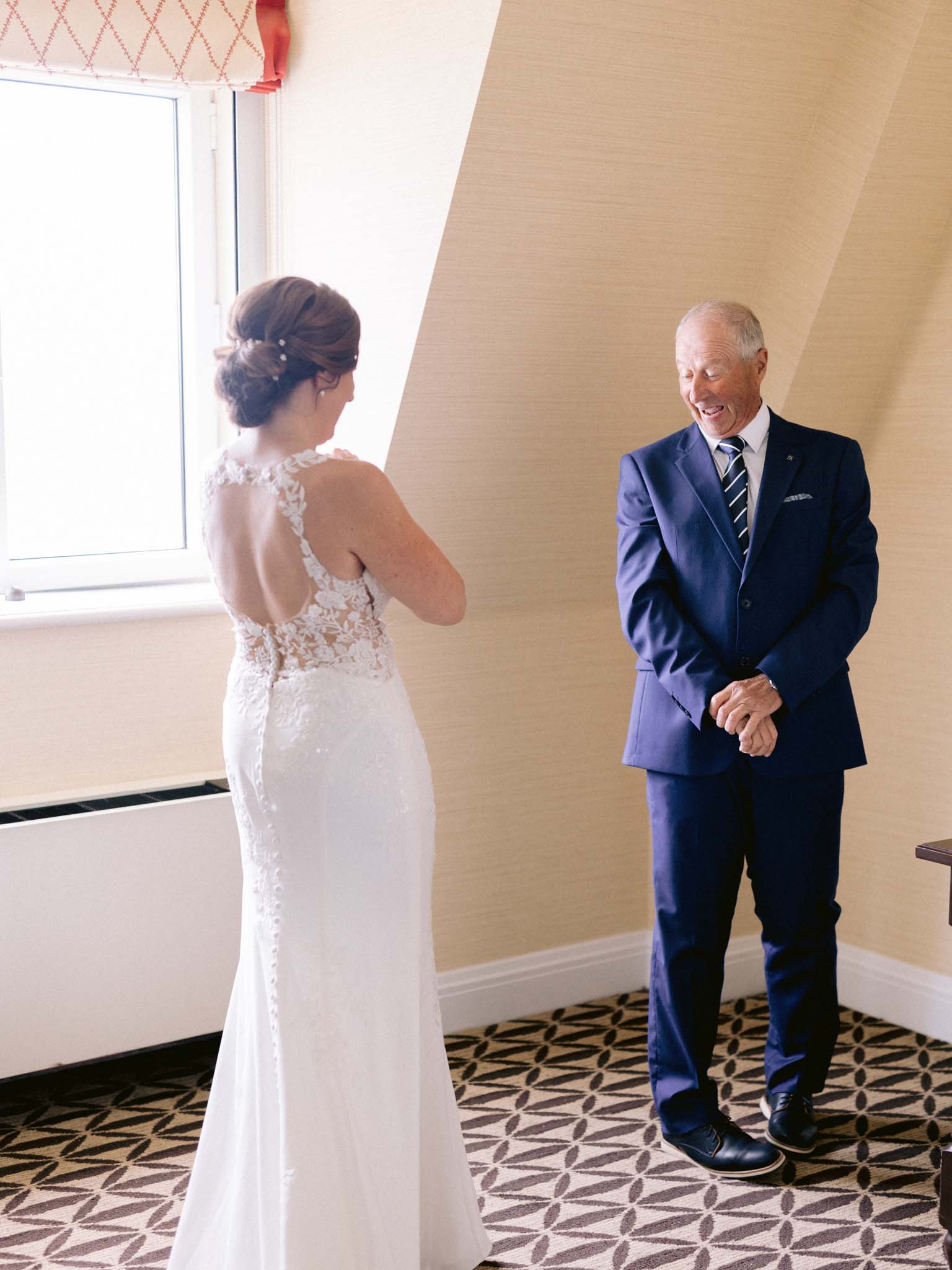 The bride's father seeing her in her gown for the first time, laughing in the hotel room