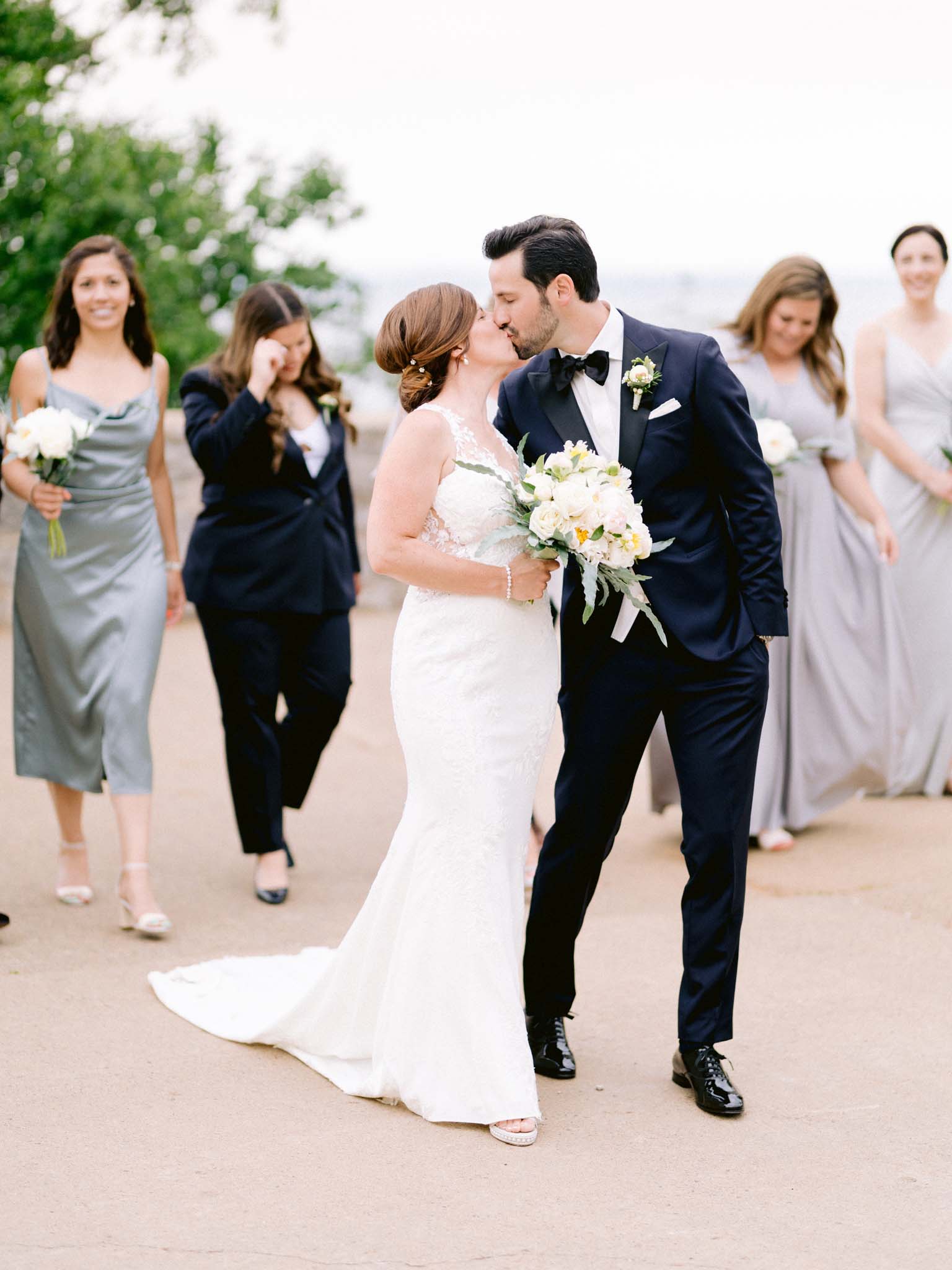 Bride and groom kissing as their wedding party walks up behind them