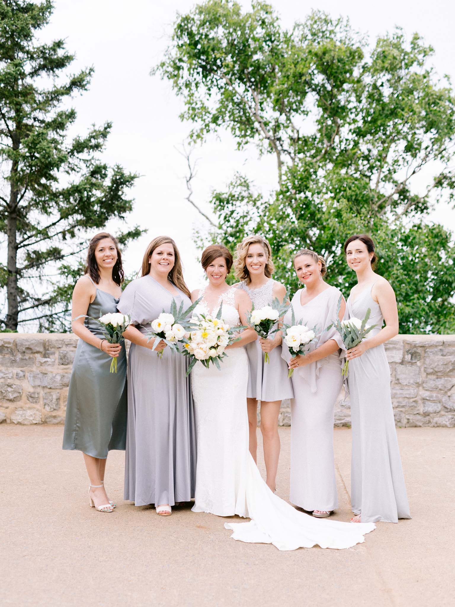 Bride with her six bridesmaids in soft grey dresses on the stone terrace above the river
