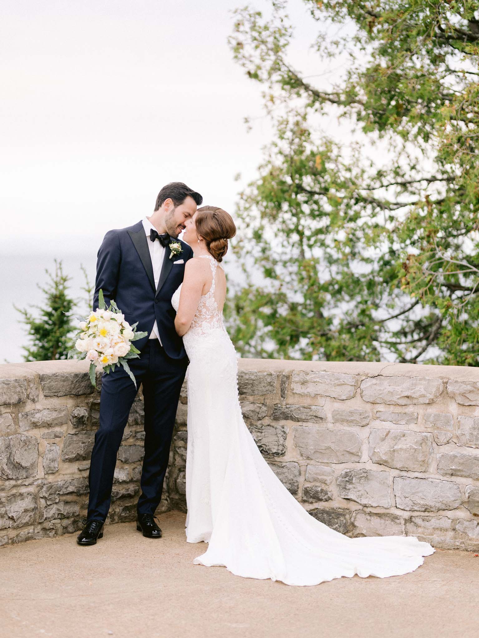 Bride and groom leaning into each other at the stone wall above the St. Lawrence