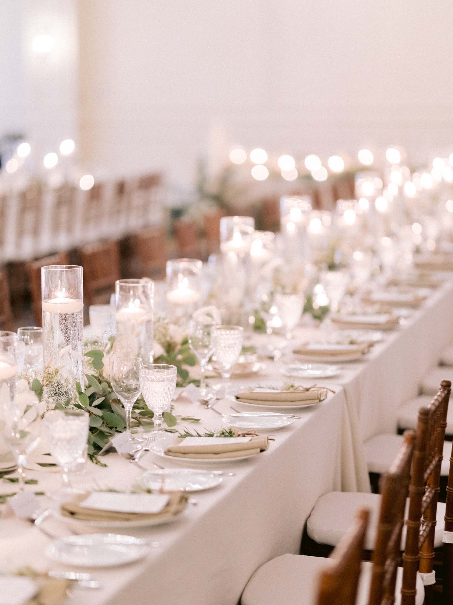 Long reception table lined with floating candles, eucalyptus and place settings