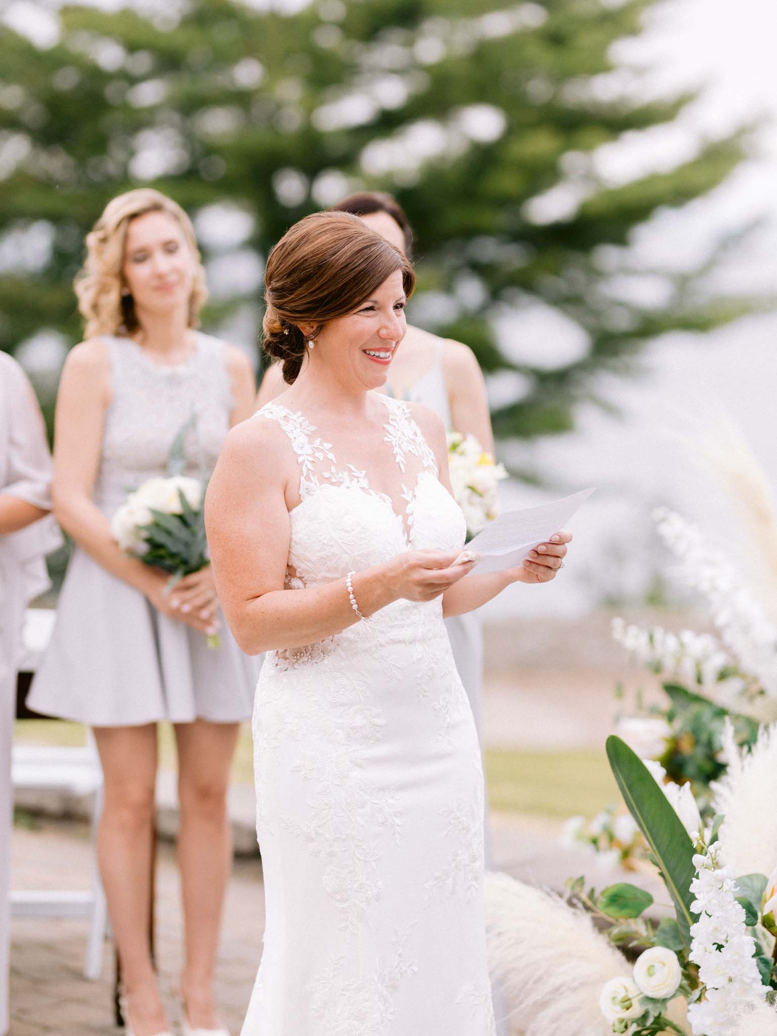 Bride smiling as she reads her vows from a folded page during the ceremony