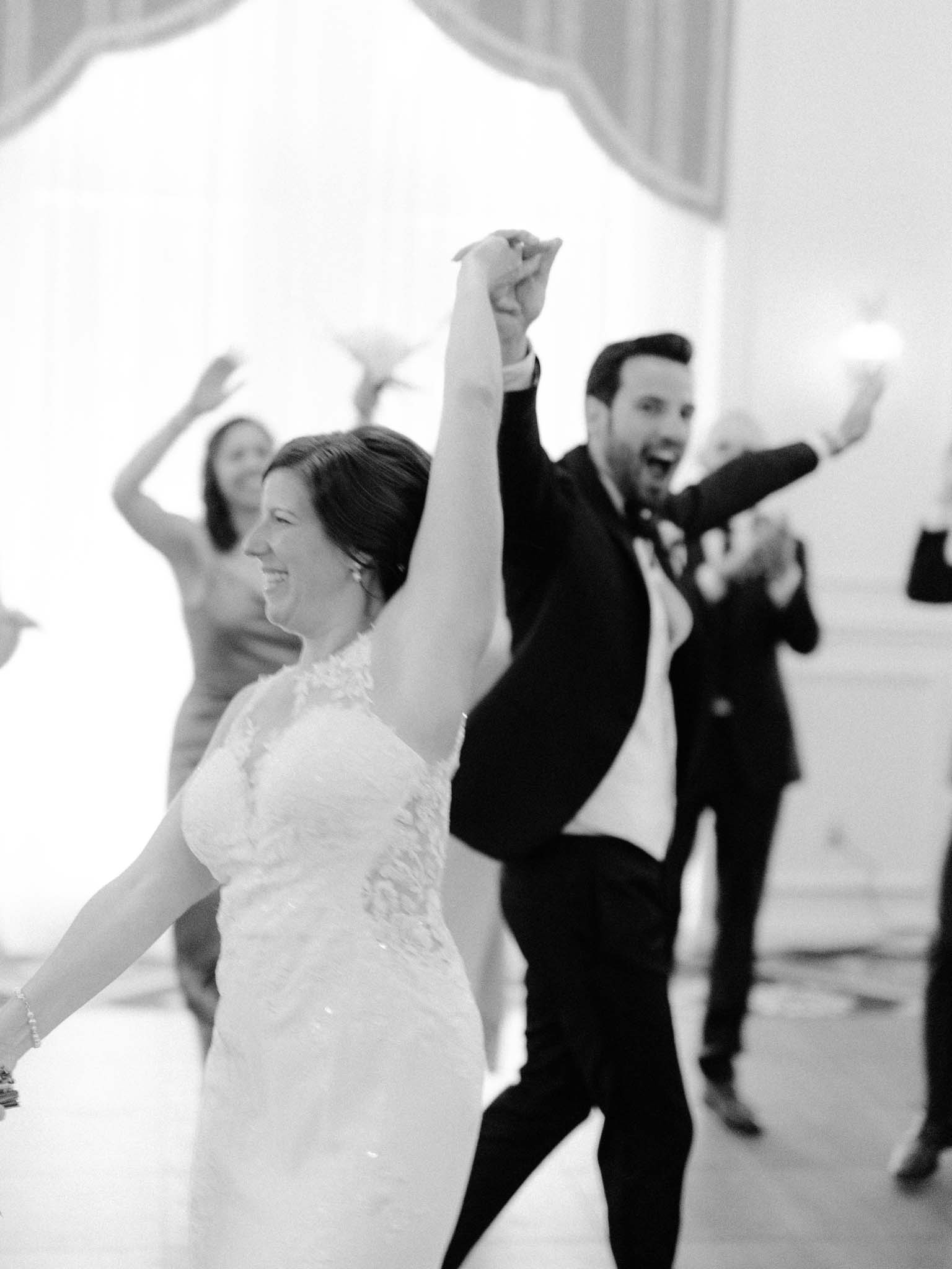 Bride and groom dancing with their arms raised as guests cheer around them