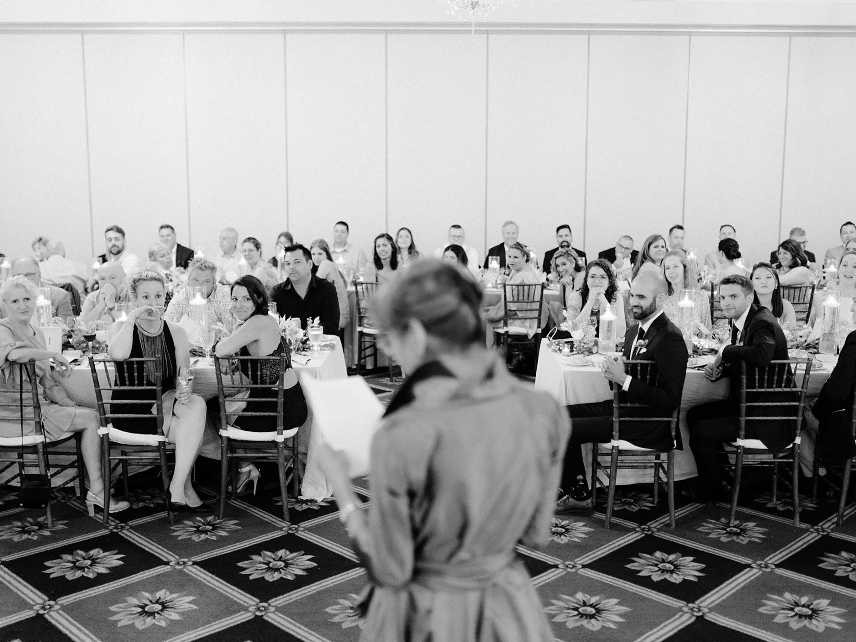 A guest giving a speech to the seated room, in black and white