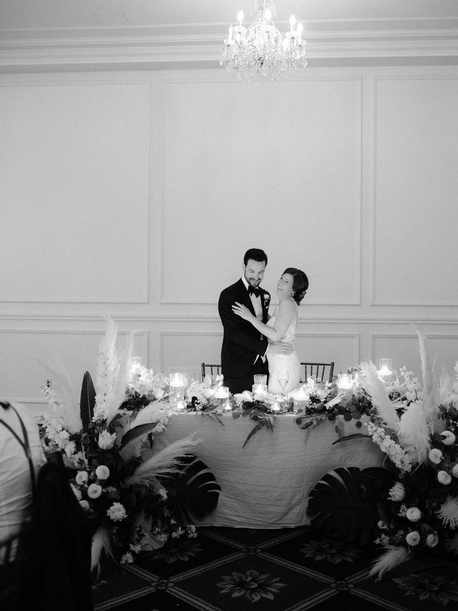Bride and groom holding each other at the head table beneath the chandelier
