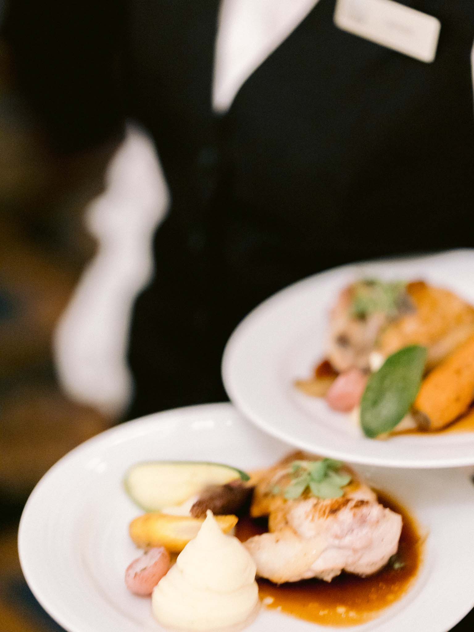 A server carrying two plates of stuffed chicken supreme through the reception
