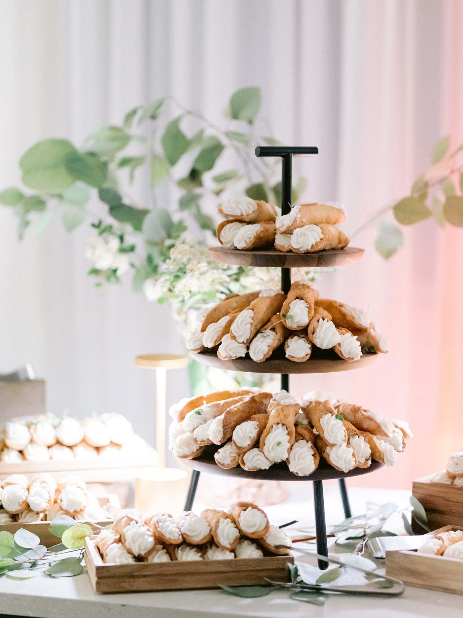 Tiered wooden stand of cream-filled cannoli on the dessert table