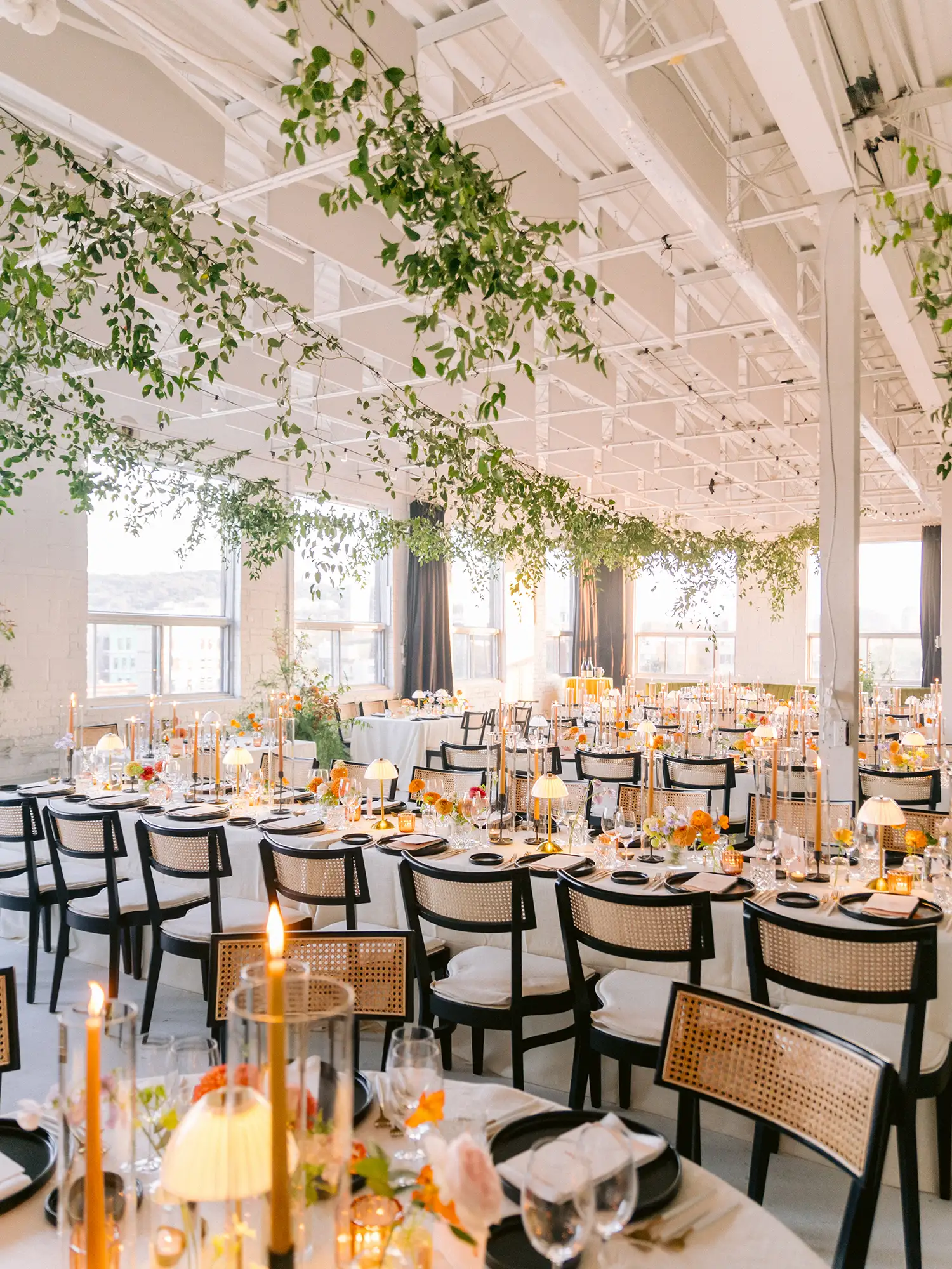 Réception à l'Espace L'Éloi à Montréal avec de la verdure suspendue au plafond blanc du loft et des chandelles ambrées sur chaque table