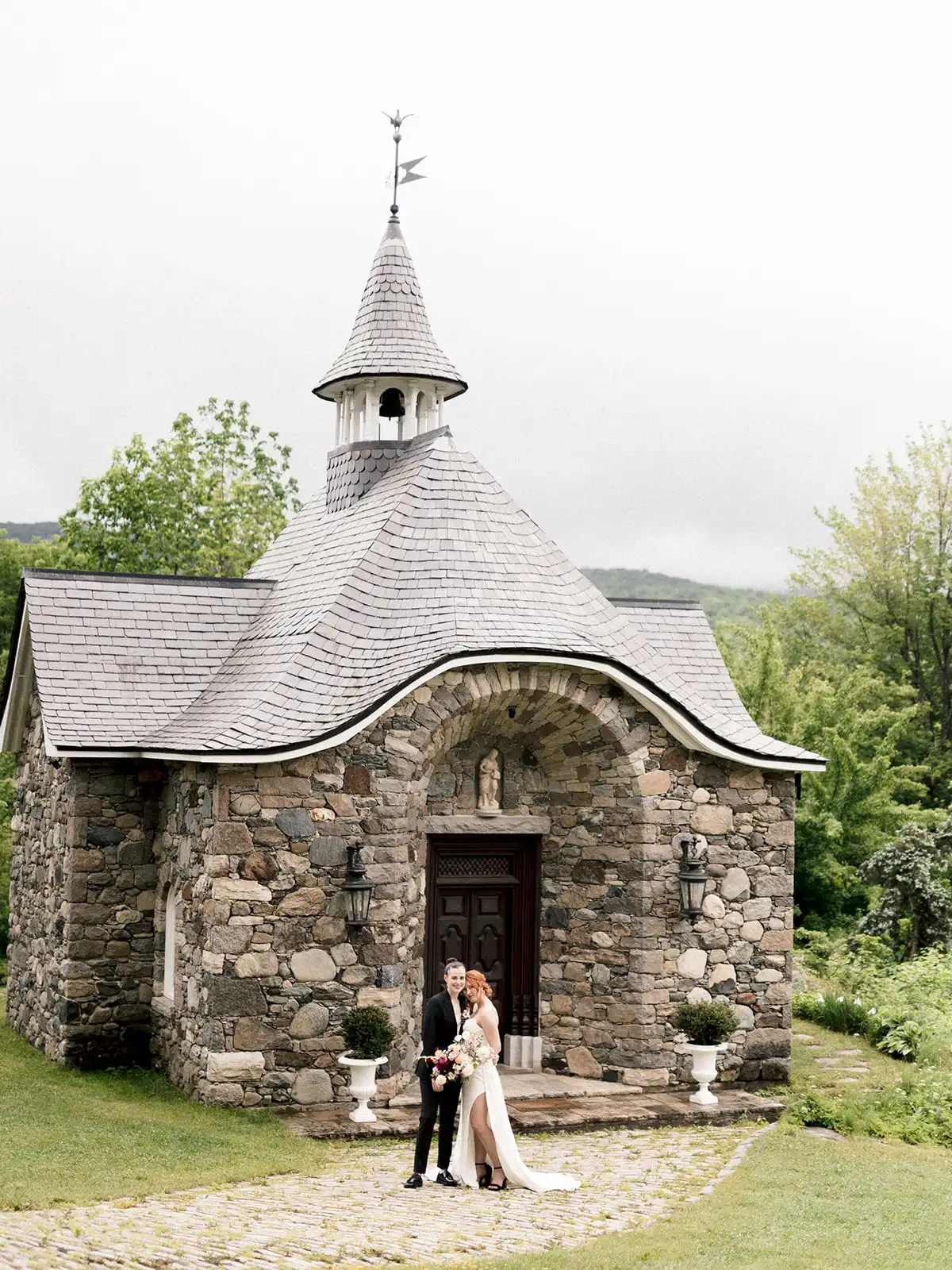 Bride and groom outside the fieldstone chapel with a shingled bell tower at Château Ste-Agnès in the Eastern Townships