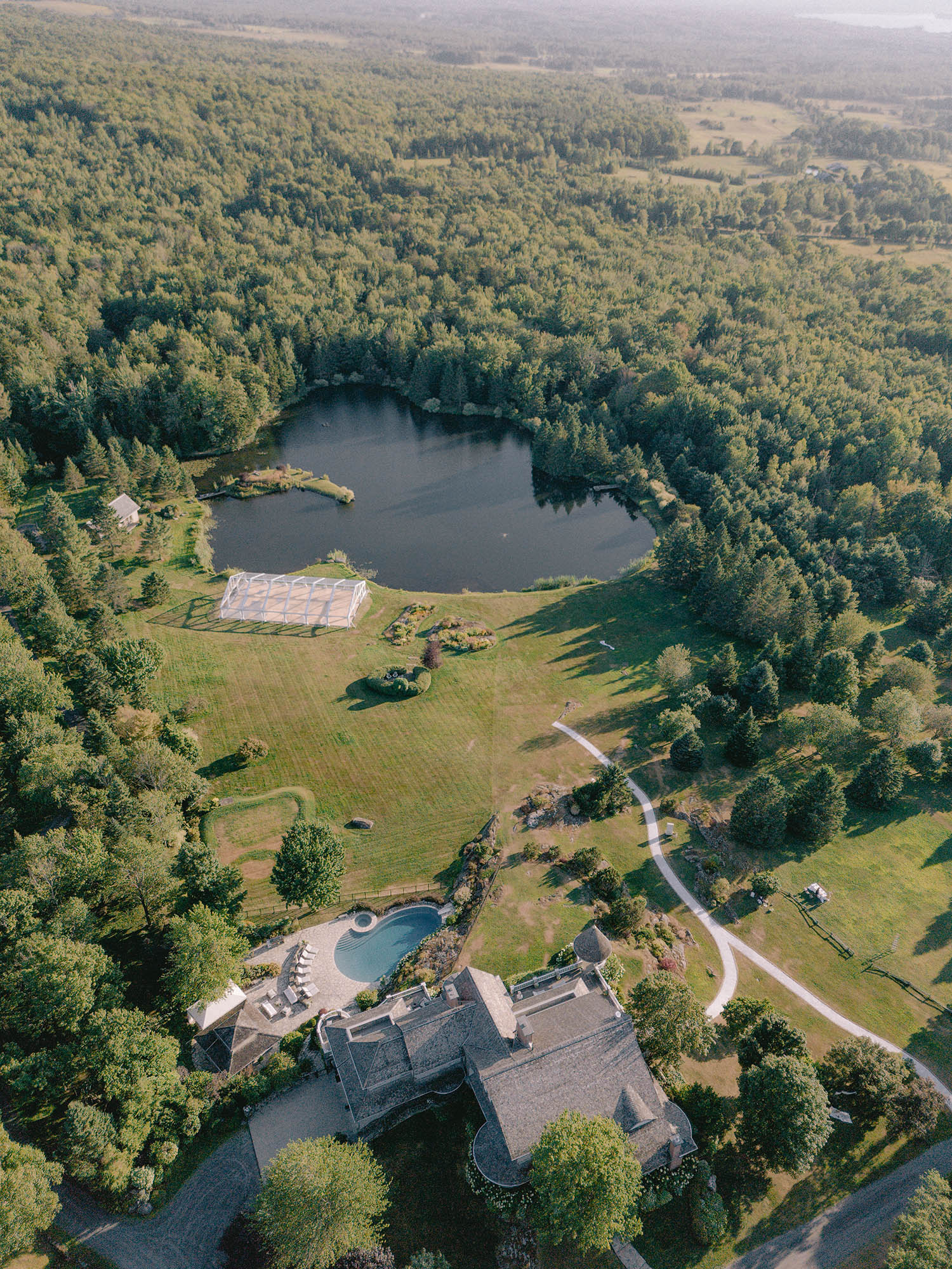 Aerial view of the Maison Bolton estate in the Eastern Townships, a clear-top tent on the lawn beside the lake and the manor above the pool