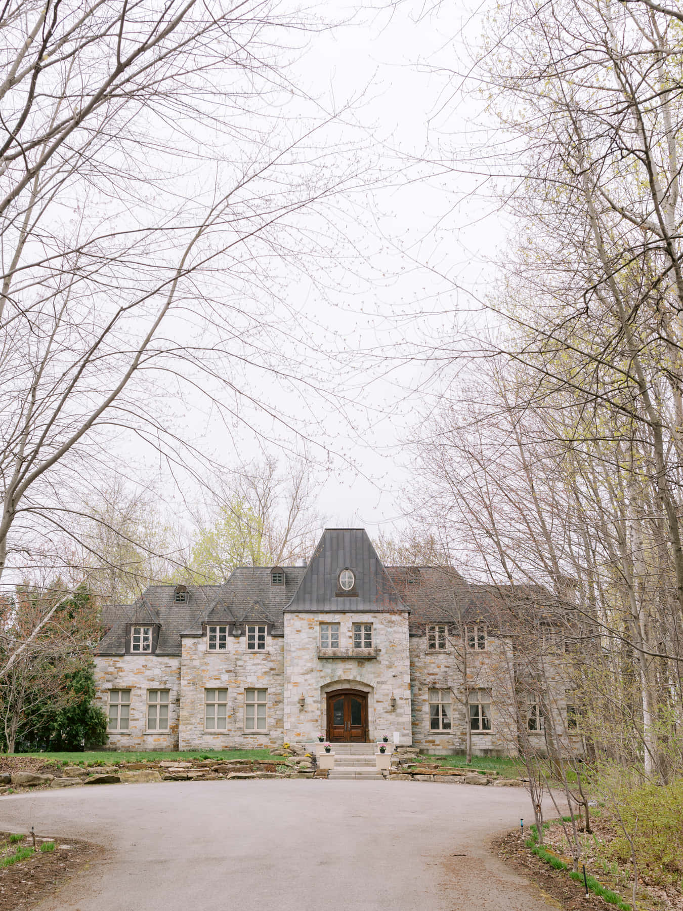 Façade de pierre du Château Taillefer Lafon au bout de son allée bordée d'arbres, au début du printemps