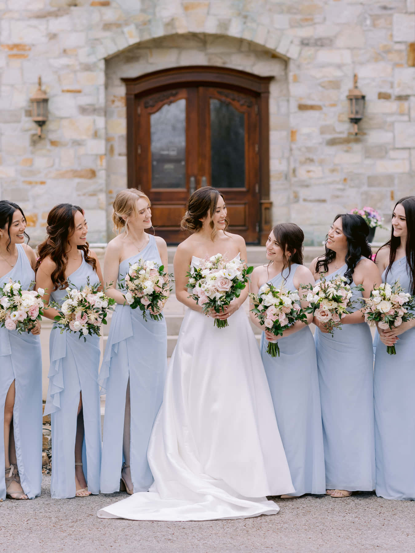 Mariée et demoiselles d'honneur tenant leurs bouquets devant les portes de bois cintrées du château