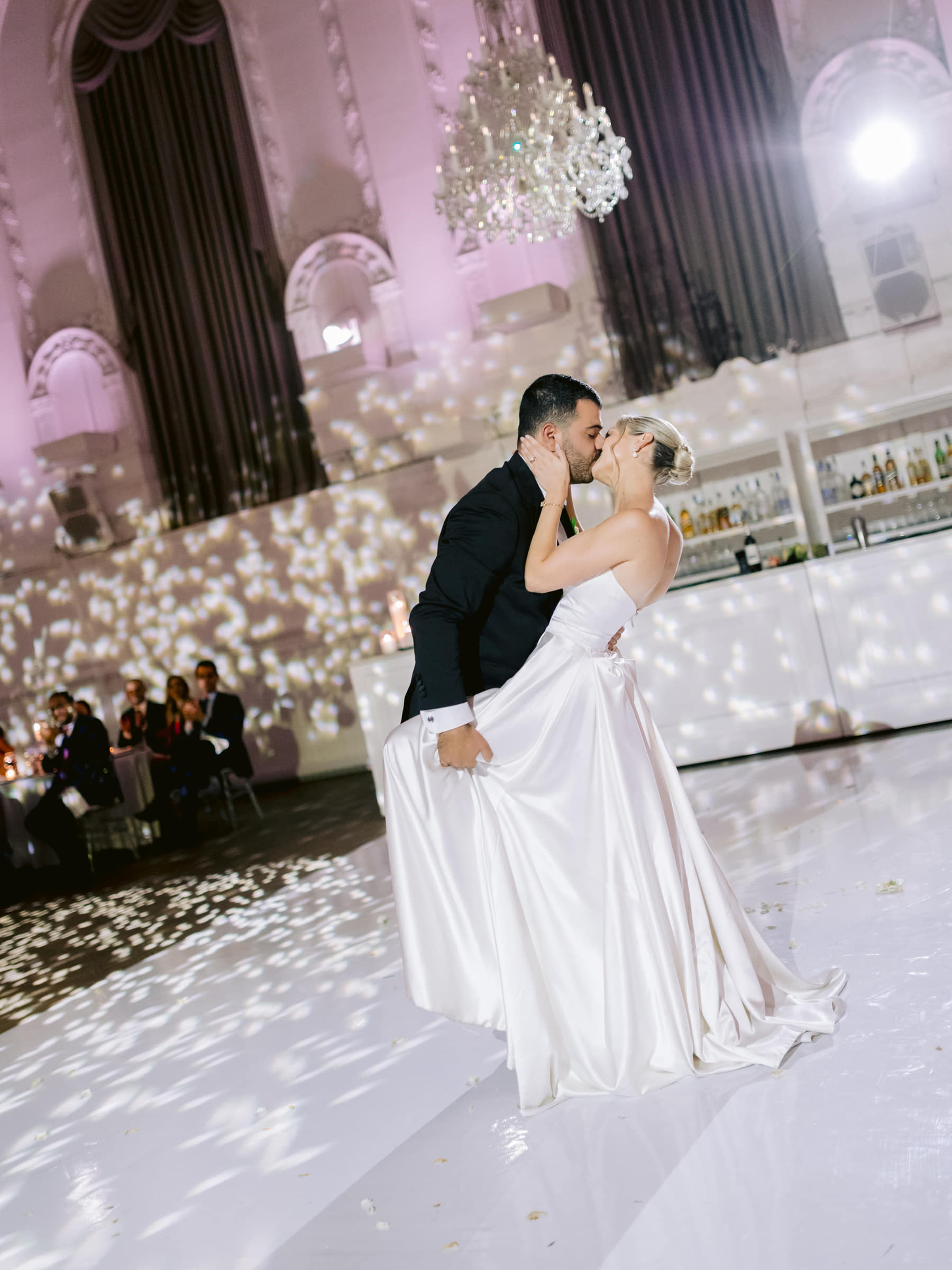 Groom dipping the bride for a kiss on the dance floor beneath a crystal chandelier at Maison Principale