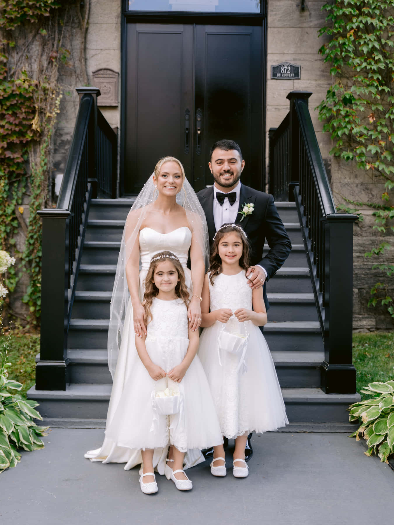 Bride and groom with two flower girls at the foot of the black stairs of one of Maison Principale's entrances