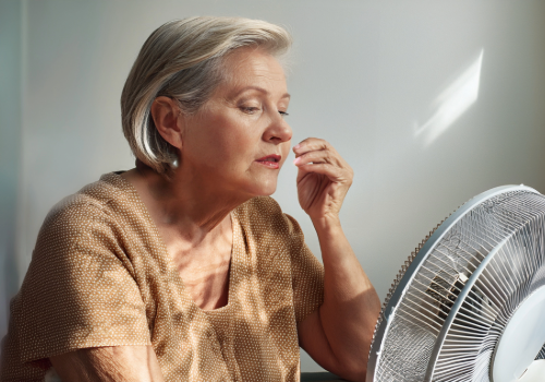 Sweating elderly person sitting in front of a fan, trying to cool off from extreme heat.