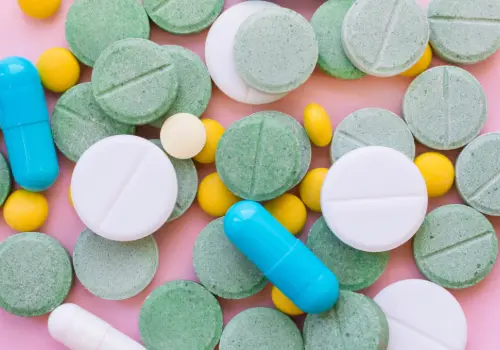 Capsule and tablet pills scattered across a pink background.