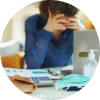 Woman at her desk with her hands on her head and a face mask beside her computer, representing feeling sick at work and deciding whether to wear a mask during recovery.