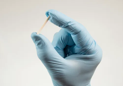 A healthcare provider wearing gloves holds a Norplant birth control implant to show its small, flexible capsules used for long-term contraception.