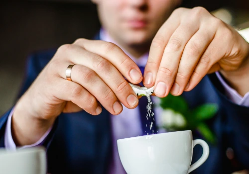 A person adds a packet of sugar-free sweetener into coffee — illustrating mindful sugar substitute use for diabetes management.