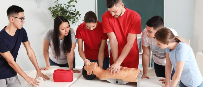 CPR instructor teaching a small group of adults how to perform hands-only chest compressions during a CPR certification class.