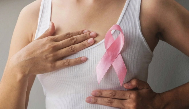 Woman wearing a white tank top with a pink breast cancer ribbon, symbolizing breast cancer awareness and support, used to represent compassionate breast cancer care at BASS Medical Group.