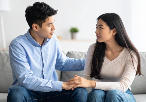 Two adults sitting together on a couch, one listening while the other speaks, conveying support and empathy.