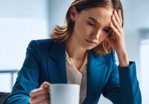 Fatigued businesswoman at work trying to stay awake by drinking coffee.