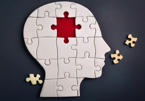 Illustration of a human head puzzle with a missing red-highlighted brain piece and three non-fitting pieces nearby, symbolizing memory loss and cognitive decline.