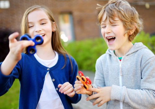 Two children using fidget spinners while sitting at a table, illustrating common attention and focus challenges associated with ADHD.