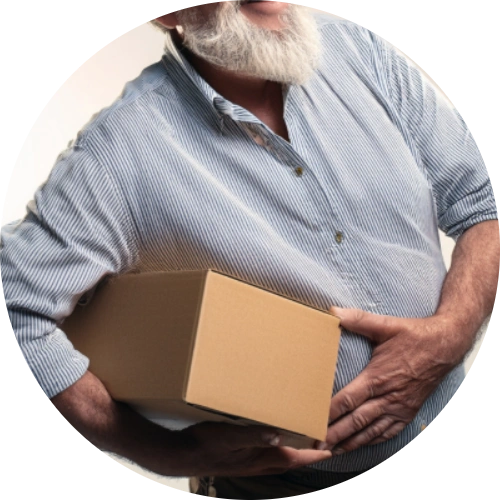 Older man grabbing his lower belly with a shipping box in front to show that he was trying to lift it & ended up with a hernia.