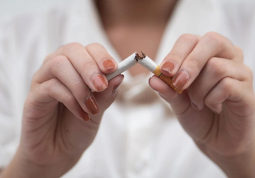 Person snapping a cigarette in half to symbolize quitting smoking and improving overall health.