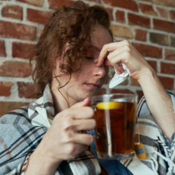 Woman with sinus inflammation, commonly called sinusitis, drinking warm tea