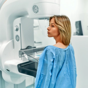  A woman in a blue robe stands before an MRI machine, preparing for a mammogram procedure