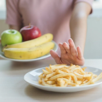 A person holds a plate of golden french fries alongside a fresh red apple, highlighting a contrast in cholesterol