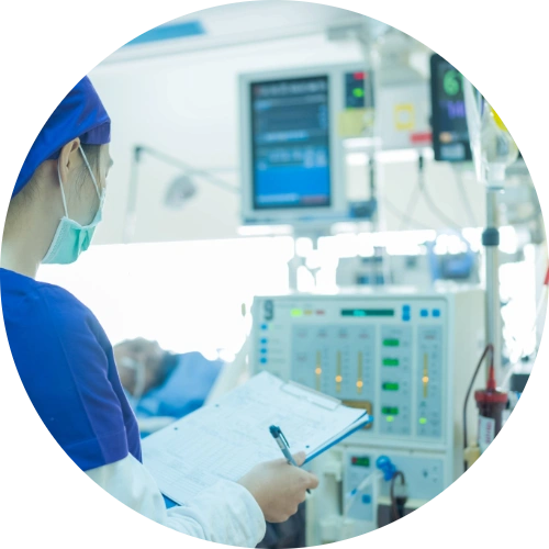 A nurse in a hospital room holds a clipboard, overseeing a patient undergoing dialysis for kidney disease.