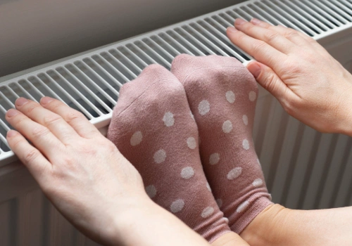 Woman warming cold feet and hands near a home radiator