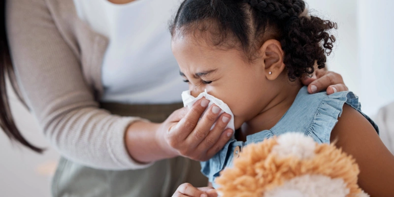 Mom swiping her child's runny nose with a tissue, consistent with common cold symptoms