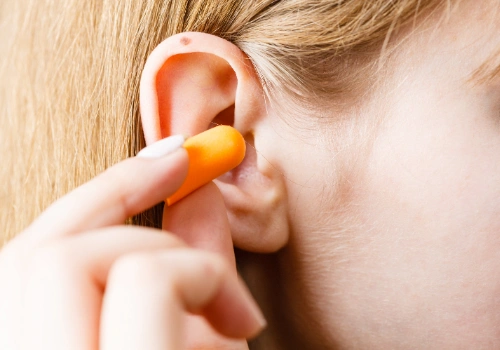 Woman inserting an orange ear plug to prevent hearing loss