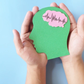 Hands hold a paper cutout of a brain with a heartbeat, symbolizing a mini stroke