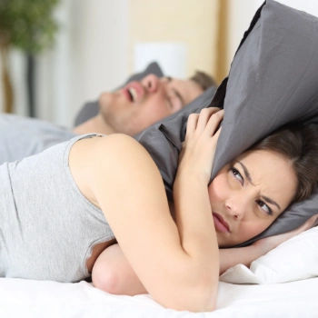 Woman using a pillow to block our her husband's snoring
