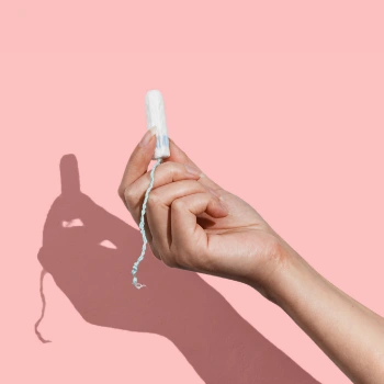 Hand holding a tampon against a pink background