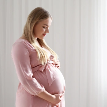 Pregnant woman in a pink robe holding her belly