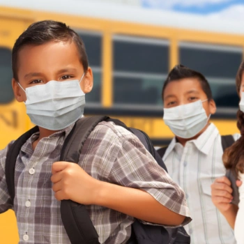 Kids wearing masks next to a school bus