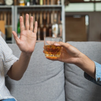 Man declining a glass of bourbon from his friend